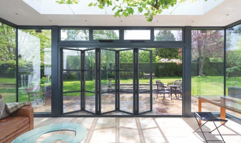 Aluco bifold doors in a conservatory, partially open with patio and garden view and sky