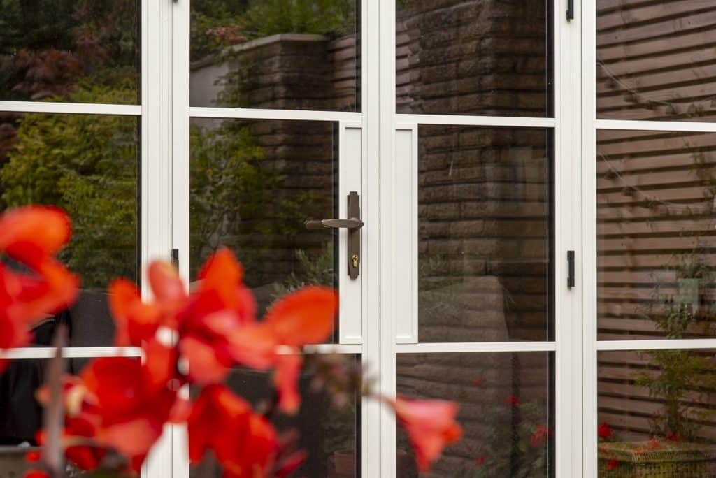 close up picture of Aluco white steel look doors behind some red flowers