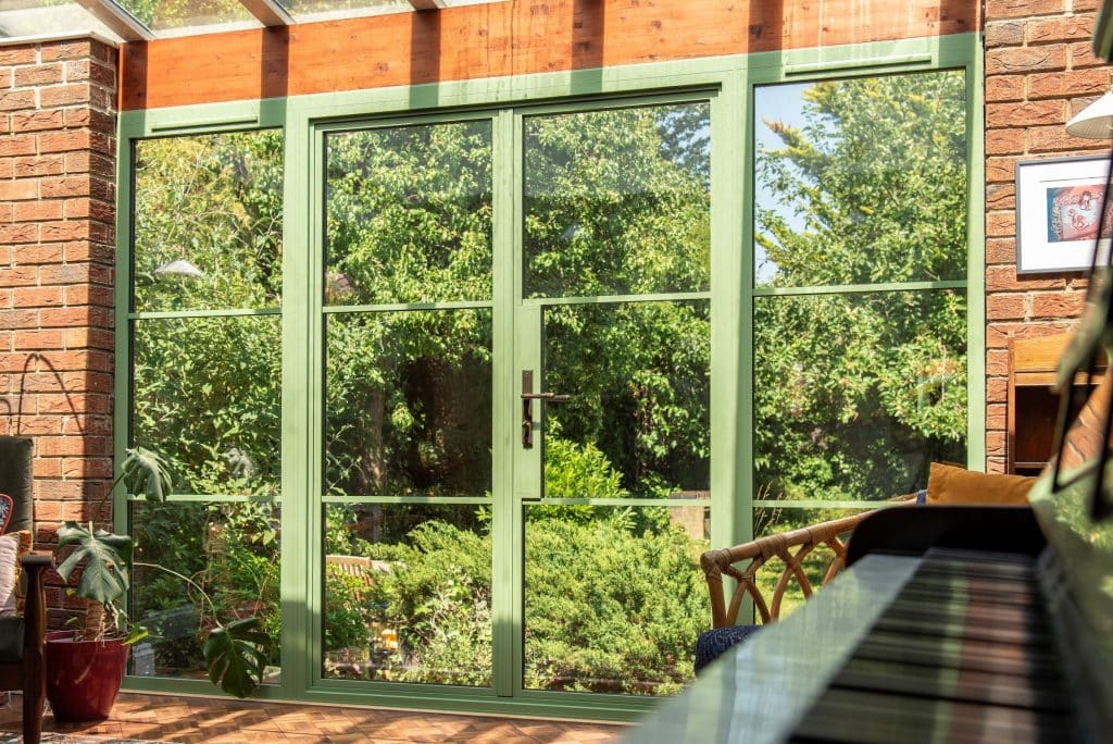Side view of Aluco steel look doors in Cambridge house in a vibrant green colour with view or a piano keyboard and garden views