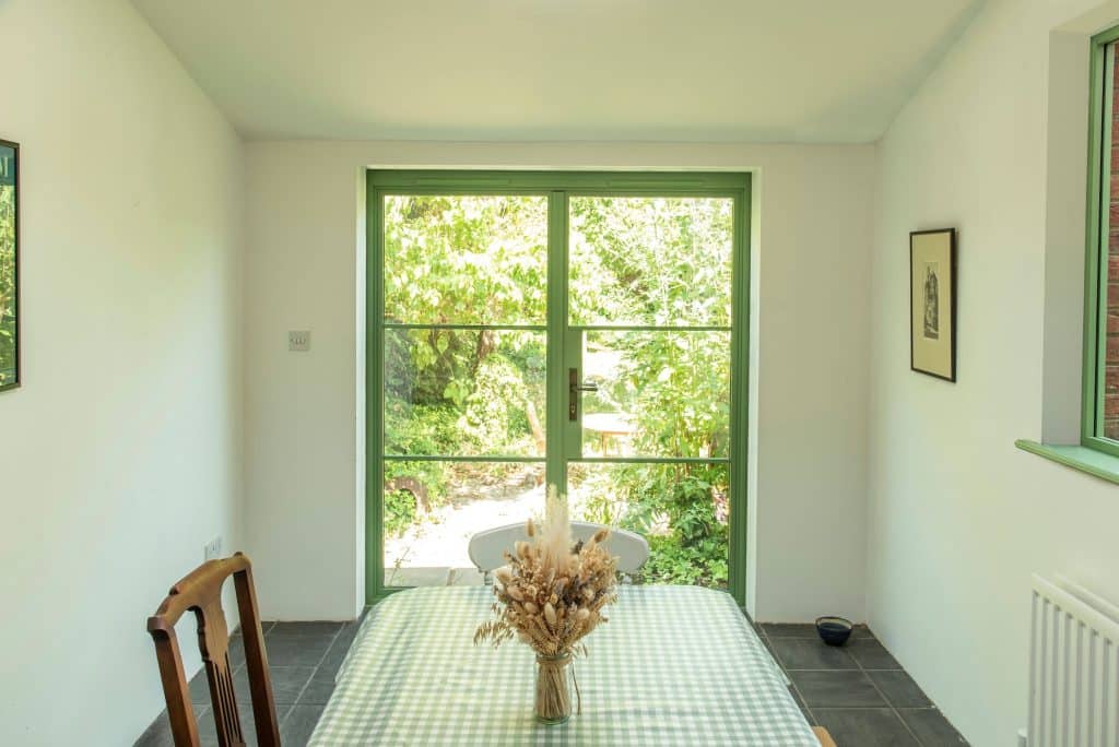 Aluco steel look doors in Green colour with garden views in a dining room.