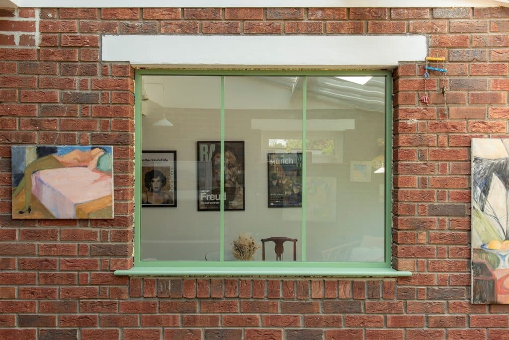 Picture of internal picture window in green finish within q brick wall and pictures either side.