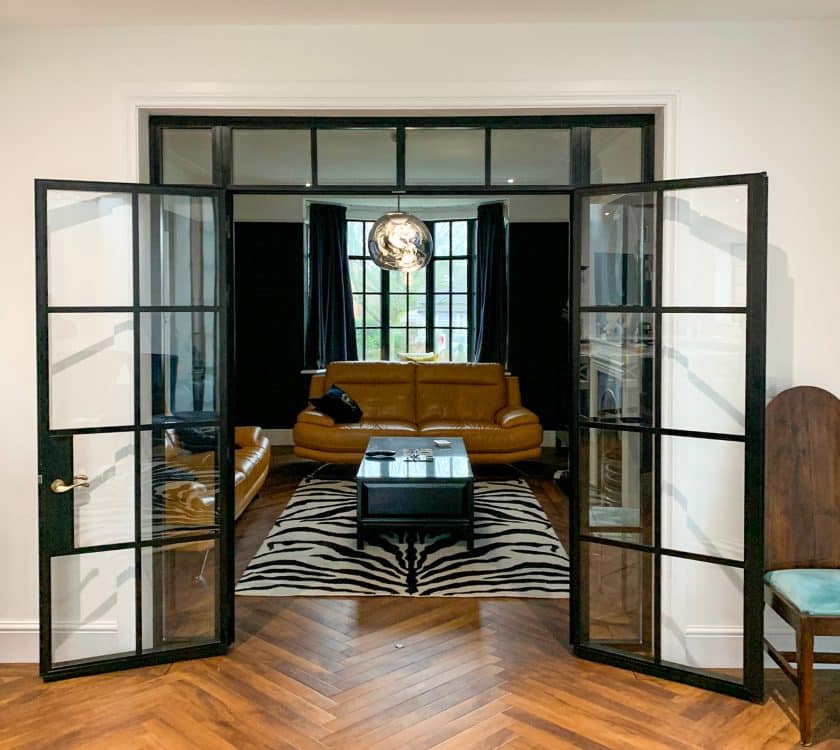 black aluco internal heritage doors fully open separating a lounge and dining area with wood floors